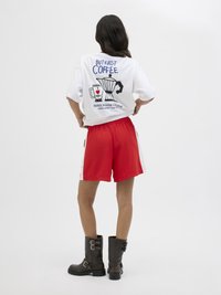 Witte T-shirt met een "Maar eerst koffie" grafiek en een illustratie van een koffiepot. Gepaard met rode shorts en zwarte enkelboots.