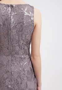 Robe en dentelle grise avec des motifs floraux en sequins, dotée d'un design sans manches et d'une fermeture éclair à l'arrière visible. Tissu texturé et détails complexes.