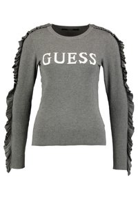 Pull gris avec détails à volants le long des manches, col rond et logo blanc audacieux "GUESS" sur le devant. Matière en maille douce.