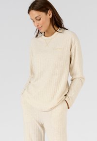 Set di loungewear a coste beige chiaro composto da un top a maniche lunghe con collo rotondo e ricamo dorato, abbinato a pantaloni coordinati.
