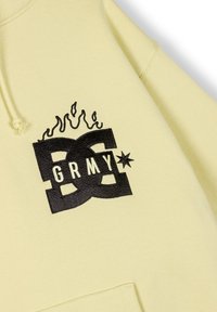 Żółta bluza z kapturem wykonana z miękkiego materiału, z wyraźnym czarnym graficznym logo z płomieniami i napisem "GRMY" na gładkiej powierzchni.