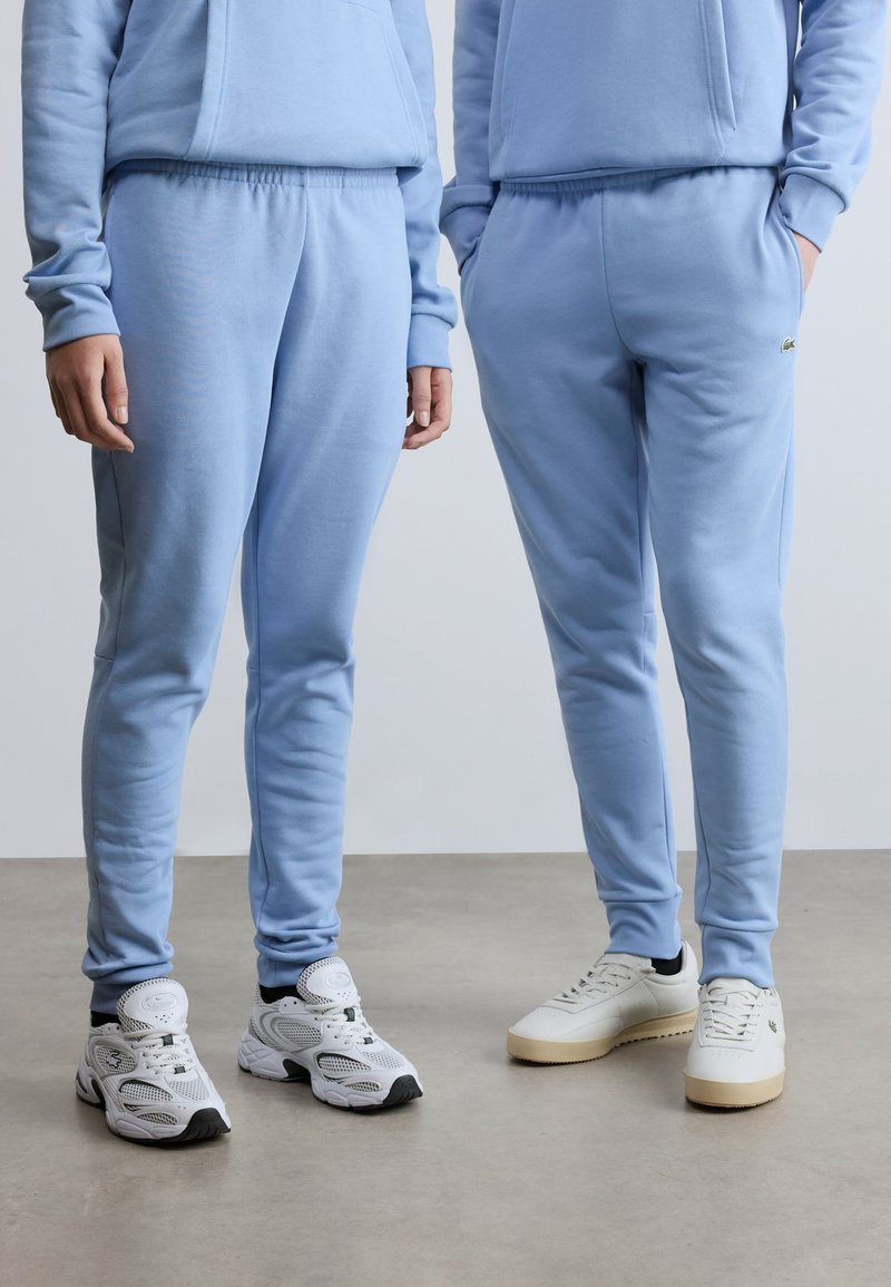 Ανοιχτό μπλε φούτερ και ταιριαστό φόρμα από μαλακό ύφασμα. Διαθέτουν ριμπ ζώνη μέσης και κεντημένο λογότυπο στα παντελόνια φόρμας. Αθλητικά παπούτσια σε λευκό και κρεμ χρώμα.