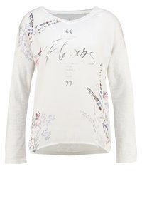 Camicia leggera a maniche lunghe di colore crema con stampa floreale e testo. Presenta un orlo arrotondato e una vestibilità rilassata. Tessuto morbido.