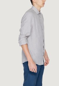 Camicia button-up grigia chiara con un sottile motivo a righe, maniche lunghe e colletto classico, abbinata a pantaloni blu scuro.
