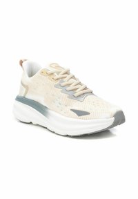 Zapatilla deportiva beige con parte superior de tela texturizada, acentos grises, suela ligera y un collar acolchado. Presenta un diseño de cordones para un ajuste seguro.