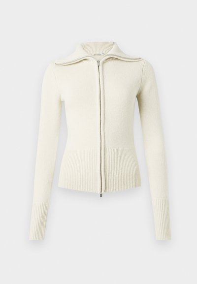 Strikket kremfarget genser med glidelås foran, ribbestrikkede mansjetter og kant. Har høy krage og glatt tekstur. Enkel, figurnær design.