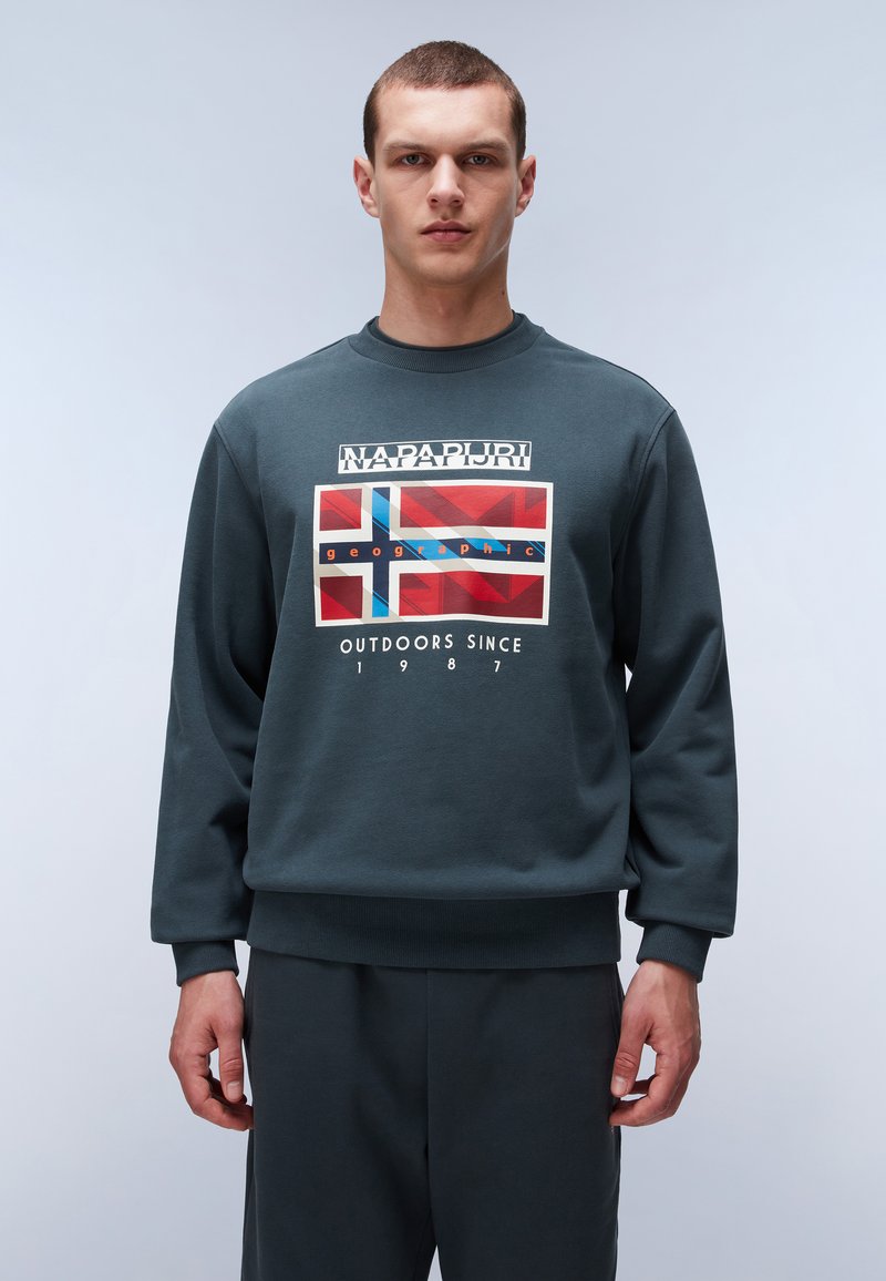 Tmavě zelená mikina se žebrovanými manžetami a lemem. Obsahuje grafický design s motivem vlajky v červené, modré a bílé barvě. Vyrobena z měkké tkaniny.