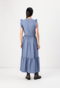 Blå chambray maxikjole med volang ermer, elastisk liv og lagdelt kant. Har en nøkkelhullåpning bak.