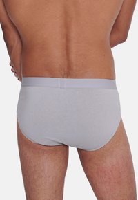 Graue Baumwollslips mit glatter Textur und elastischem Bund, enganliegendem Design und minimalen Nähten, getragen auf einem nackten Oberkörper.