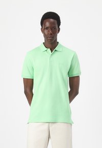 Light green polo shirt made of cotton, featuring a collar, short sleeves, and a subtle logo on the chest. Smooth texture, fitted design.