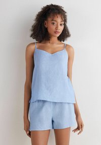 Lichtblauw, geribbeld tanktop met dunne bandjes en een V-hals, gecombineerd met bijpassende shorts. Zachte textuur en losse pasvorm voor comfort.