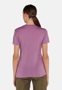 T-shirt viola a maniche corte in un morbido tessuto testurizzato con scollatura rotonda e vestibilità rilassata, abbinato a pantaloni verde chiaro.
