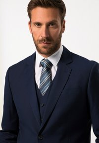 Navy-Anzug mit tailliertem Blazer, passendem Weste und weißem Hemd, ergänzt durch eine gestreifte blaue Krawatte. Glatter Stoff und maßgeschneiderter Schnitt.