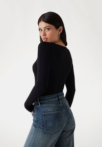 Black long-sleeve bodysuit paired with high-waisted blue denim jeans. Smooth fabric texture, form-fitting design, and classic style.