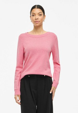 Maglione rosa a maglia con scollatura rotonda, maniche lunghe, polsini a costine e una vestibilità rilassata, indossato sopra pantaloni neri. Texture liscia.