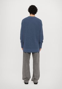 Maglione blu lavorato a maglia con una texture a coste, spalle abbassate e una vestibilità ampia. Abbinato a pantaloni larghi grigi in un tessuto morbido.