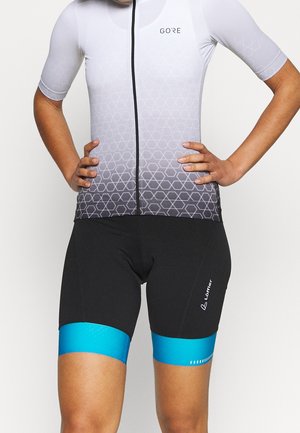 Persoon die een wielershirt draagt met een wit-grijs verloop en geometrisch patroon en zwarte wielershorts met felblauwe beenbanden.
