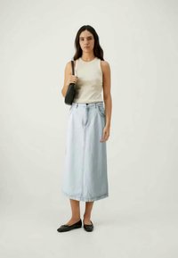 Fustă maxi din denim albastru deschis cu o talie înaltă, combinată cu un top bez cu mâneci scurte. O geantă neagră și pantofi ortopedici completează ținuta.