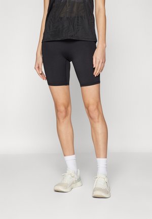 Sorte treningsshorts med en glatt tekstur, med midt-lår lengde og enkel design. Båret med lyse treningssko og hvite sokker.