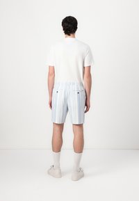 Shorts rayés bleu clair et blanc pour homme avec une taille élastique, deux poches arrière et une coupe décontractée, assortis à un t-shirt blanc et des baskets.