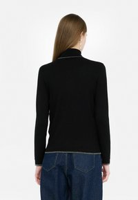 Zwarte lange mouwen top met een hoge kraag, voorzien van een metallic rand langs de halslijn en de onderzoom, gedragen met blauwe jeans.