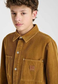 Bruine corduroy Overhemd met een klassiek kraag, twee borstzakken, drukknoopsluitingen en een leren merkpatch op de linker zak.
