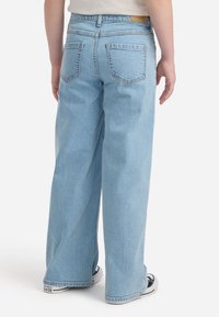 Jeans a gamba larga di colore blu chiaro con un lavaggio medio, dotati di cinque tasche, cuciture visibili e un tessuto in denim leggermente texturizzato.