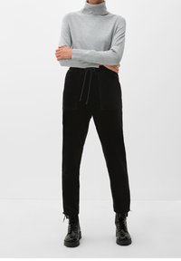 Pull à col cheminée gris, style ajusté, associé à un pantalon en velours côtelé noir taille haute avec deux poches avant et un cordon de serrage ajustable. Bottes noires à lacets.