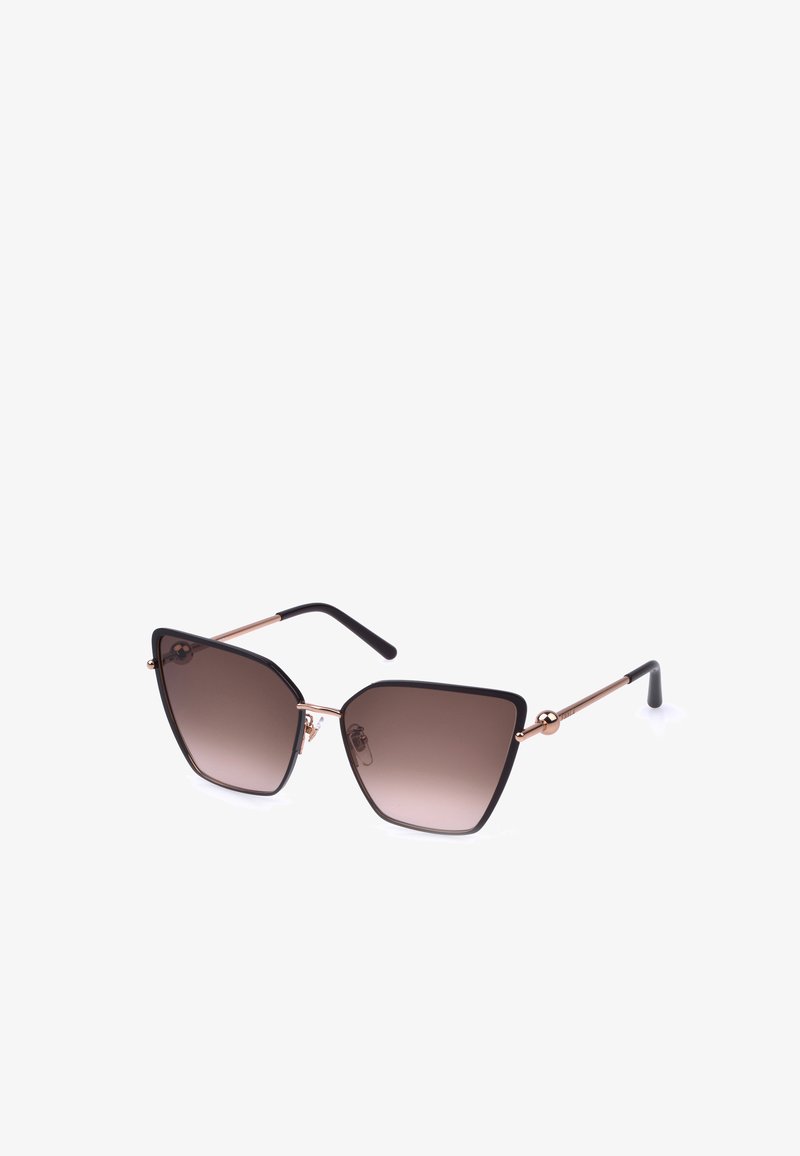Lunettes de soleil forme œil de chat avec montures noires, verres marron dégradés et branches fines dorées avec embouts noirs sur fond blanc.