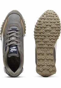 Graue und beigefarbene PumaSneaker, von oben und von der Sohle gezeigt, mit strukturiertem Gummi-Außensohle mit kreisförmigen Griffen und schnürbarem Wildleder-Obermaterial.
