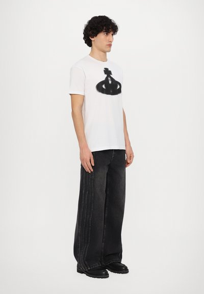 Weißes T-Shirt mit einem schwarzen Grafikdesign; kombiniert mit lockeren, schwarzen Jeans aus Denim mit seitlichen Nähten und klobigen schwarzen Stiefeln.