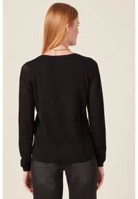 Schwarzer Pullover mit solidem Rücken und strukturierten, offenen Strickärmeln. Das Design umfasst einen runden Halsausschnitt und eine figurbetonte Silhouette.