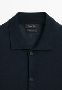 Marinblå cashmere-tröja med vikkrage, fem knappar med svarta knappar, samt en mjuk och fin struktur. Märkesskylten är synlig.