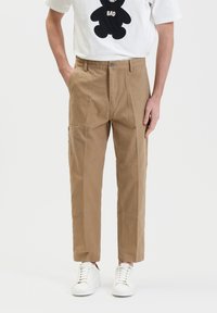 Beige chino's met een relaxte pasvorm, voorzien van twee zijzakken, een knoopsluiting en een soepel katoen. Gecombineerd met witte sneakers.