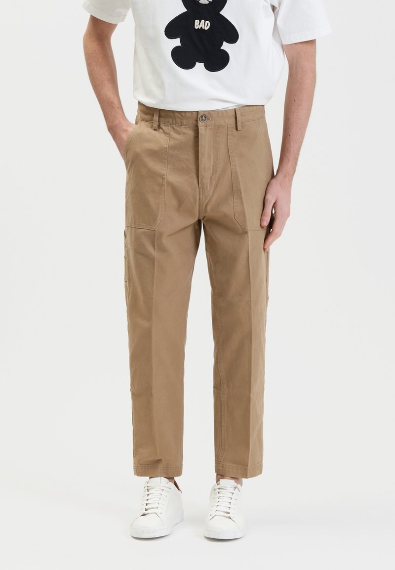 Beige chino's met een relaxte pasvorm, voorzien van twee zijzakken, een knoopsluiting en een soepel katoen. Gecombineerd met witte sneakers.
