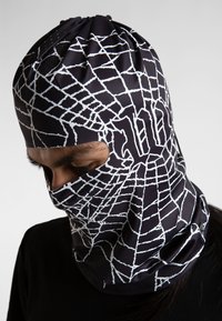 Balaclava negra hecha de tela elástica, con un diseño de patrón de telaraña blanca. El diseño incluye cortes para los ojos y un ajuste ceñido alrededor de la cabeza.
