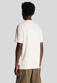 Kortærmet ivory t-shirt lavet af blødt bomuld, med en klassisk rund hals og lige pasform, båret med olivengrønne cargo-bukser.