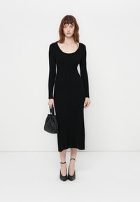 Black ribbed knit dress with long sleeves and a scoop neckline, mid-calf length. Paired with a black handbag and black heels.