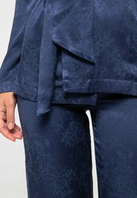 Ensemble deux pièces bleu marine avec une texture satinée. Le haut présente un devant drapé et un détail de nœud ; le bas est à jambes droites avec un motif subtil.