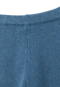 Jersey de punto con una textura suave, que presenta un escote redondeado y un color azul. Los detalles incluyen una costura central en la parte posterior.