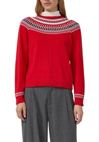 Czerwony sweter z okrągłym dekoltem i białym oraz czarnym wzorem dekoracyjnym przy kołnierzu. Długie rękawy i prążkowany dół. Noszony z szarymi spodniami.