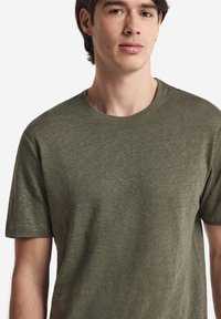 Olivgrön t-shirt med kort ärm, tillverkad av mjukt, strukturerat tyg, med klassisk rund halsringning och avslappnad passform.