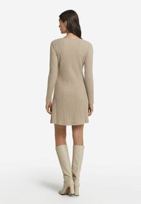Strickkleid in Beige mit gerippter Textur, langen Ärmeln und einem ausgestellten Saum, kombiniert mit kniehohen beigen Stiefeln.