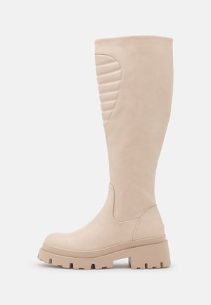 Botte beige montant jusqu'au genou avec semelle épaisse et détail rembourré côtelé sur le haut du mollet, conçue pour un port décontracté et élégant.