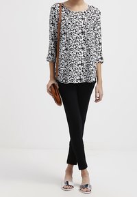 Svart och vit blommönstrad topp med trekvartslånga ärmar, ihop med svarta slim-fit byxor och silverfärgade halkskor, bärande en brun handväska.