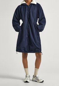 Námorně modrý lehký kabát s límcem z umělé kožešiny, elastickými rukávy, stahovacími pasem a bočními kapsami. Disponuje plným zipem.