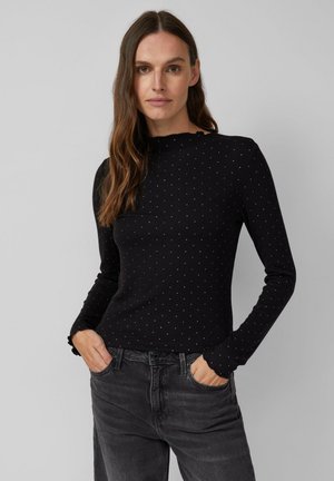 Czarny top z długim rękawem o rypanej teksturze i białymi kropkami. Posiada subtelny falbaniasty dekolt i dopasowaną sylwetkę. Połączony z szarymi dżinsami.