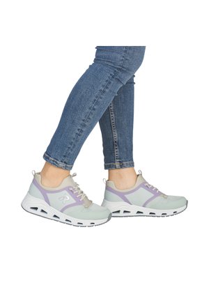 Persoon die lichtgrijze en lavendelkleurige sportieve sneakers met witte zolen en een blauwe spijkerbroek draagt, op de tenen staat tegen een witte achtergrond.