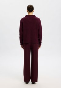 Pull en maille bordeaux avec un col montant, associé à un pantalon large assorti. Le tissu a une finition texturée et côtelée.