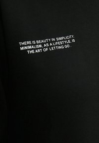 Svart bomullsduk med vit text. Texten lyder: "Det finns skönhet i enkelhet. Minimalism, som livsstil, är konsten att släppa taget."